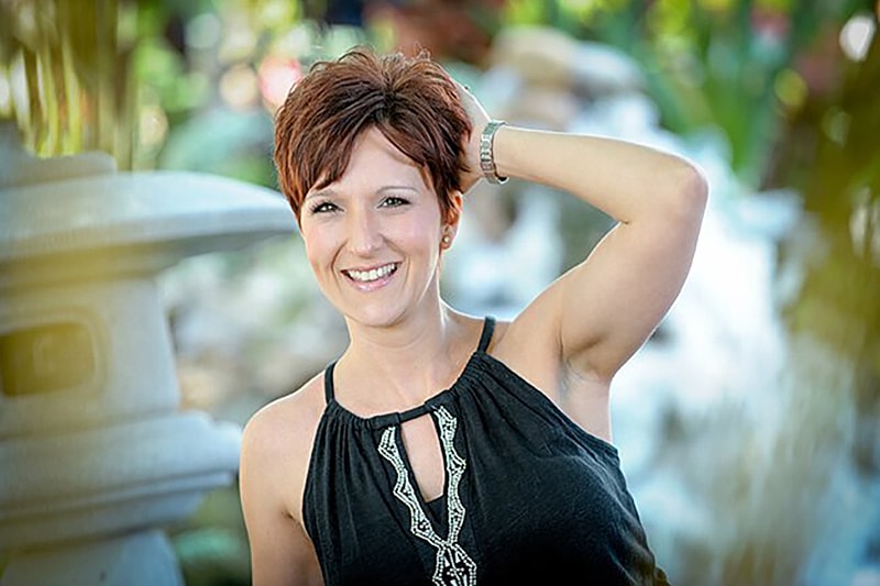 Smiling woman posing outdoors near water feature.