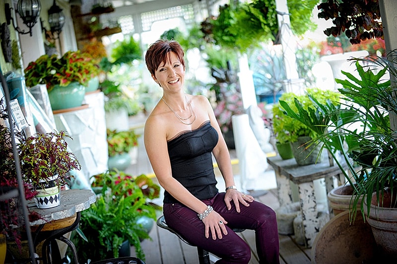 Smiling woman surrounded by lush greenery.