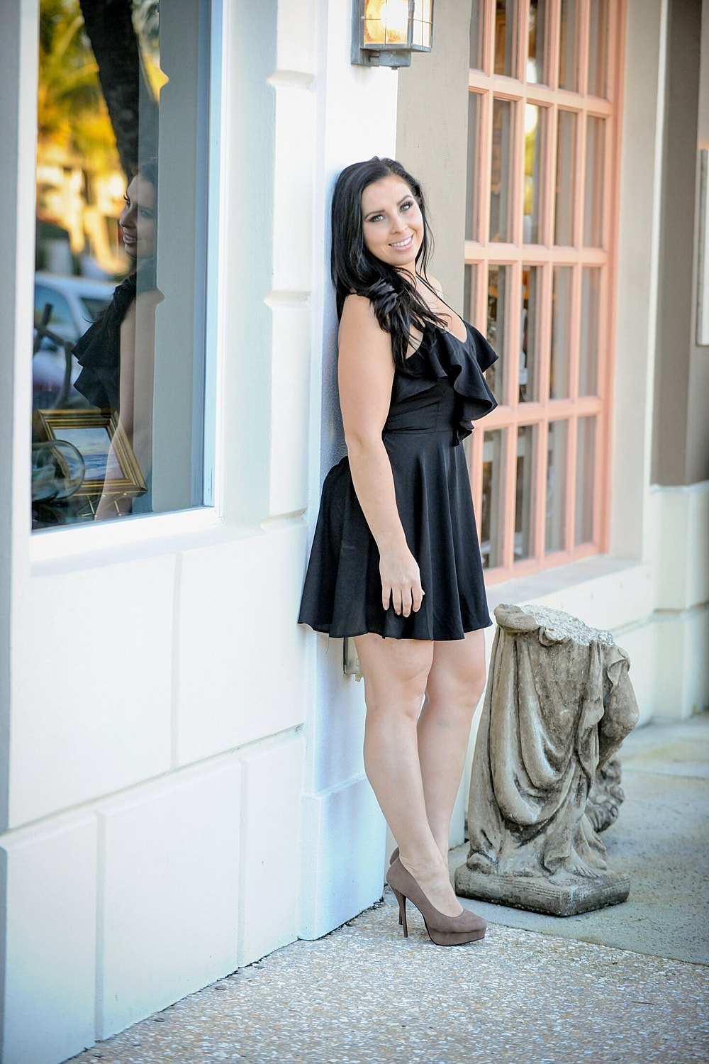 Woman in black dress poses by a building.