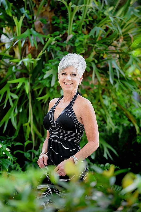 Smiling woman in black dress among greenery.