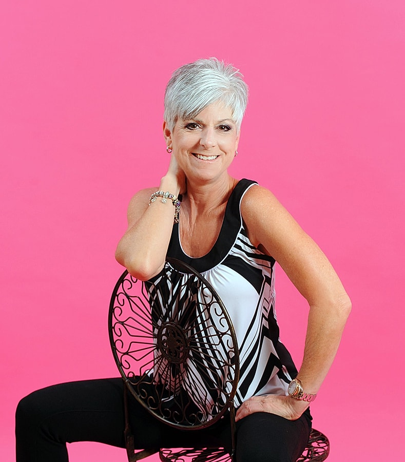 Woman with short hair posing against pink background.