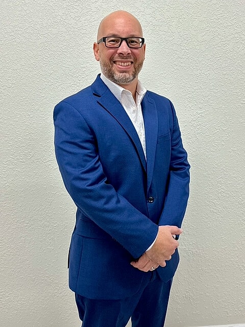 Smiling man in blue suit against plain background.
