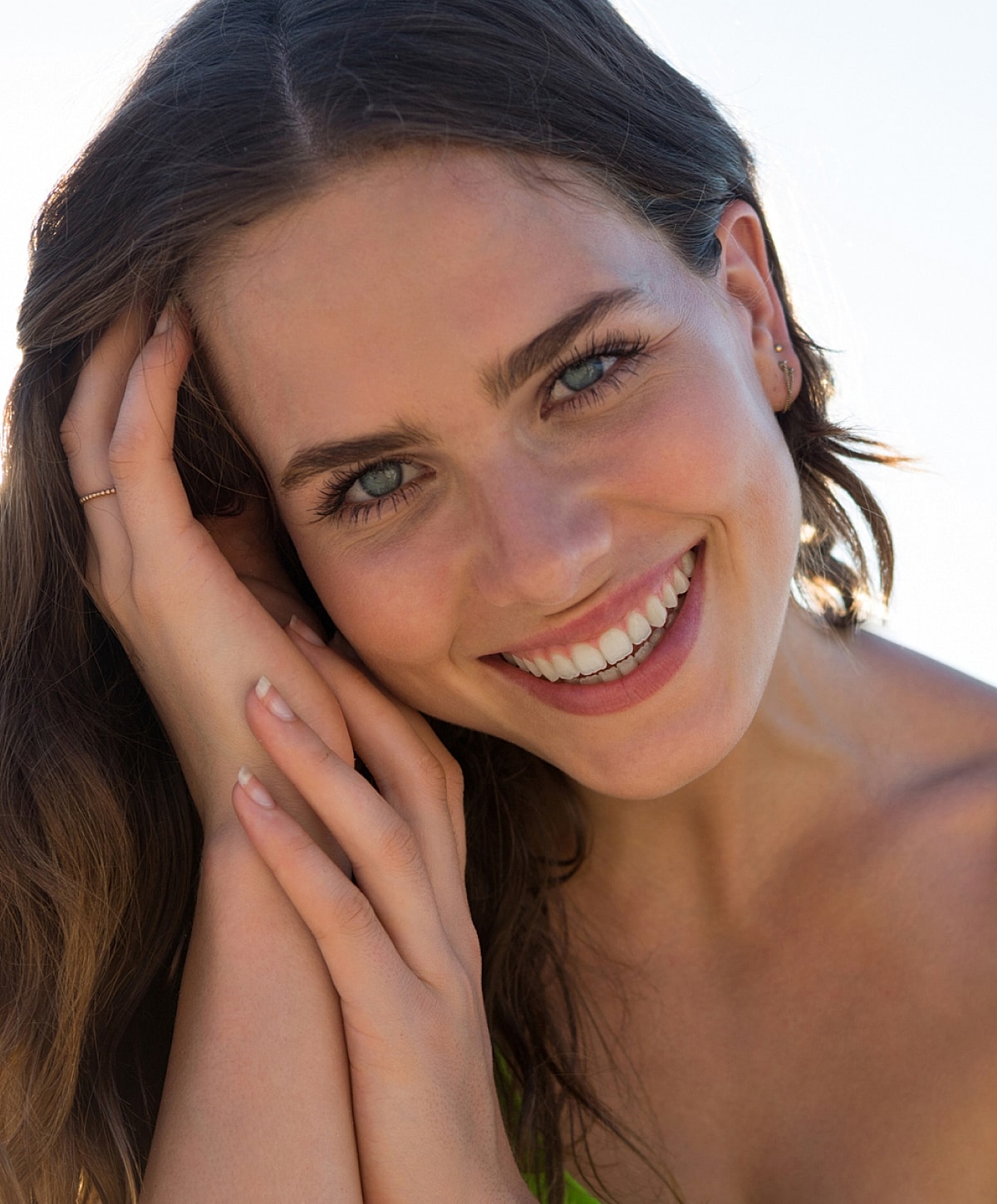 Smiling woman with long hair and hands on face.