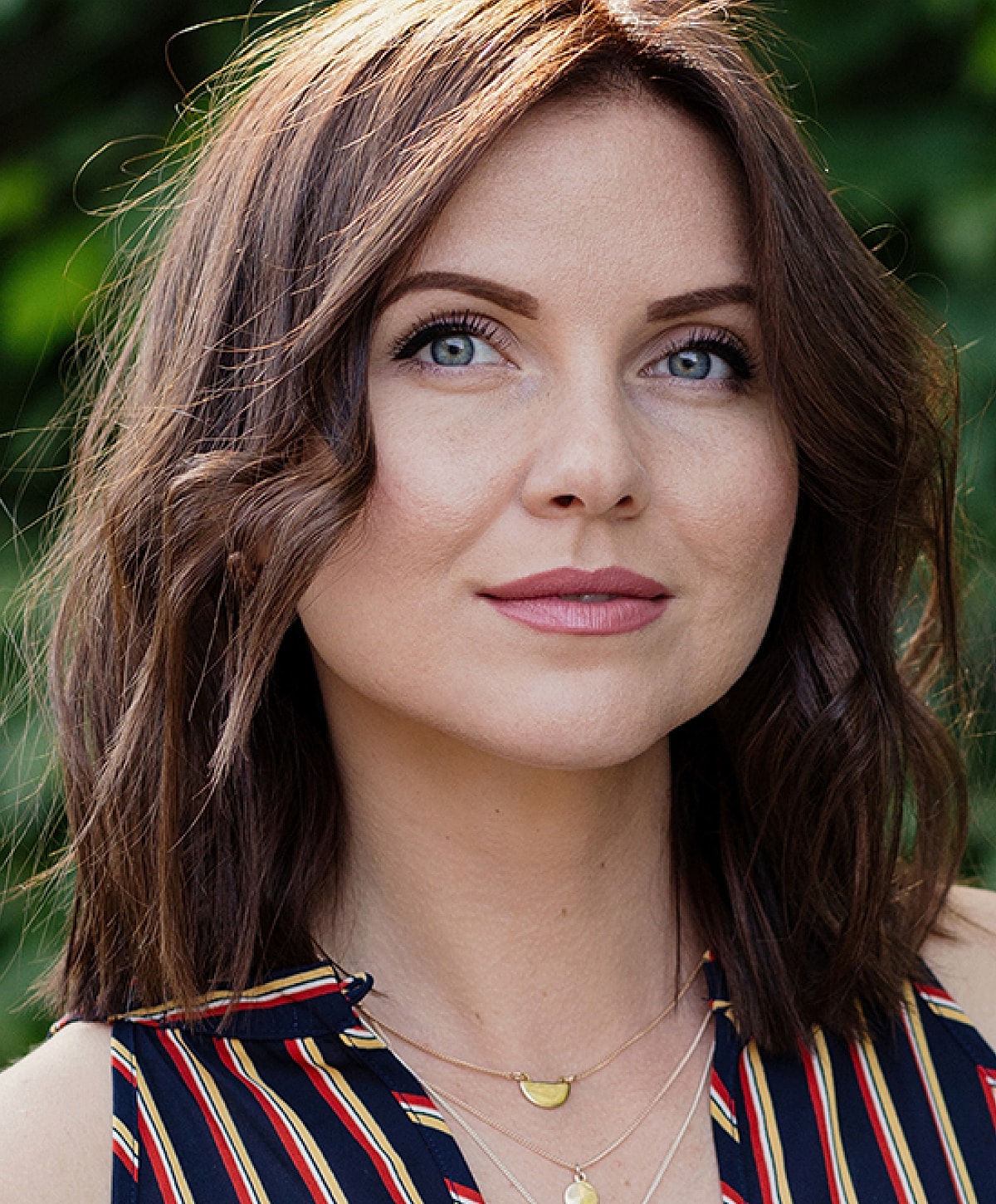 Woman smiling with glasses in a garden.