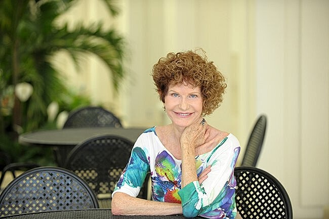 Smiling woman with curly hair in colorful blouse.