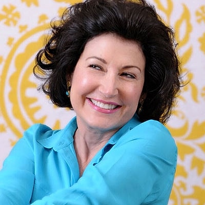 Smiling woman in blue shirt against yellow background.