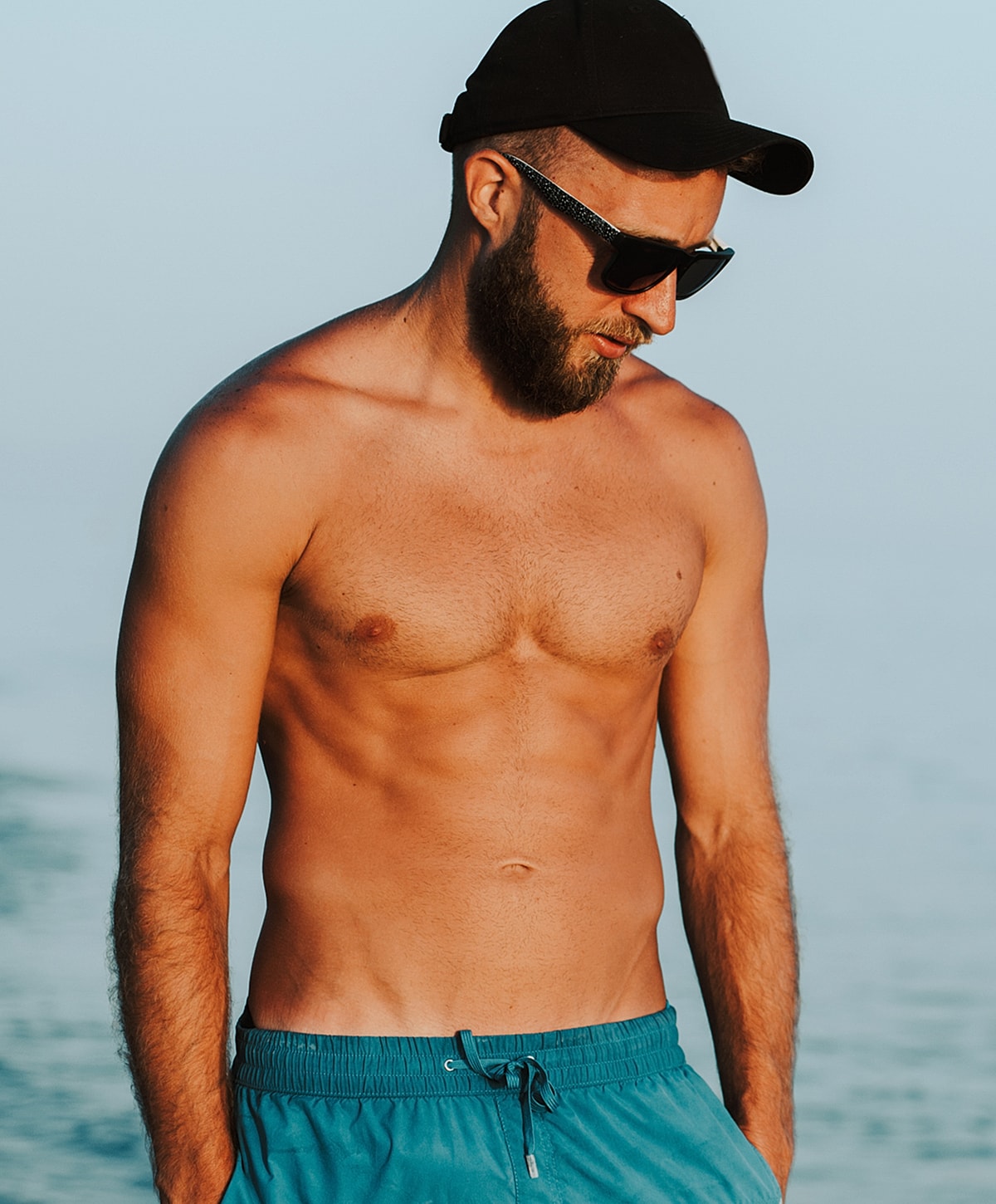 Man at the beach wearing sunglasses and shorts.