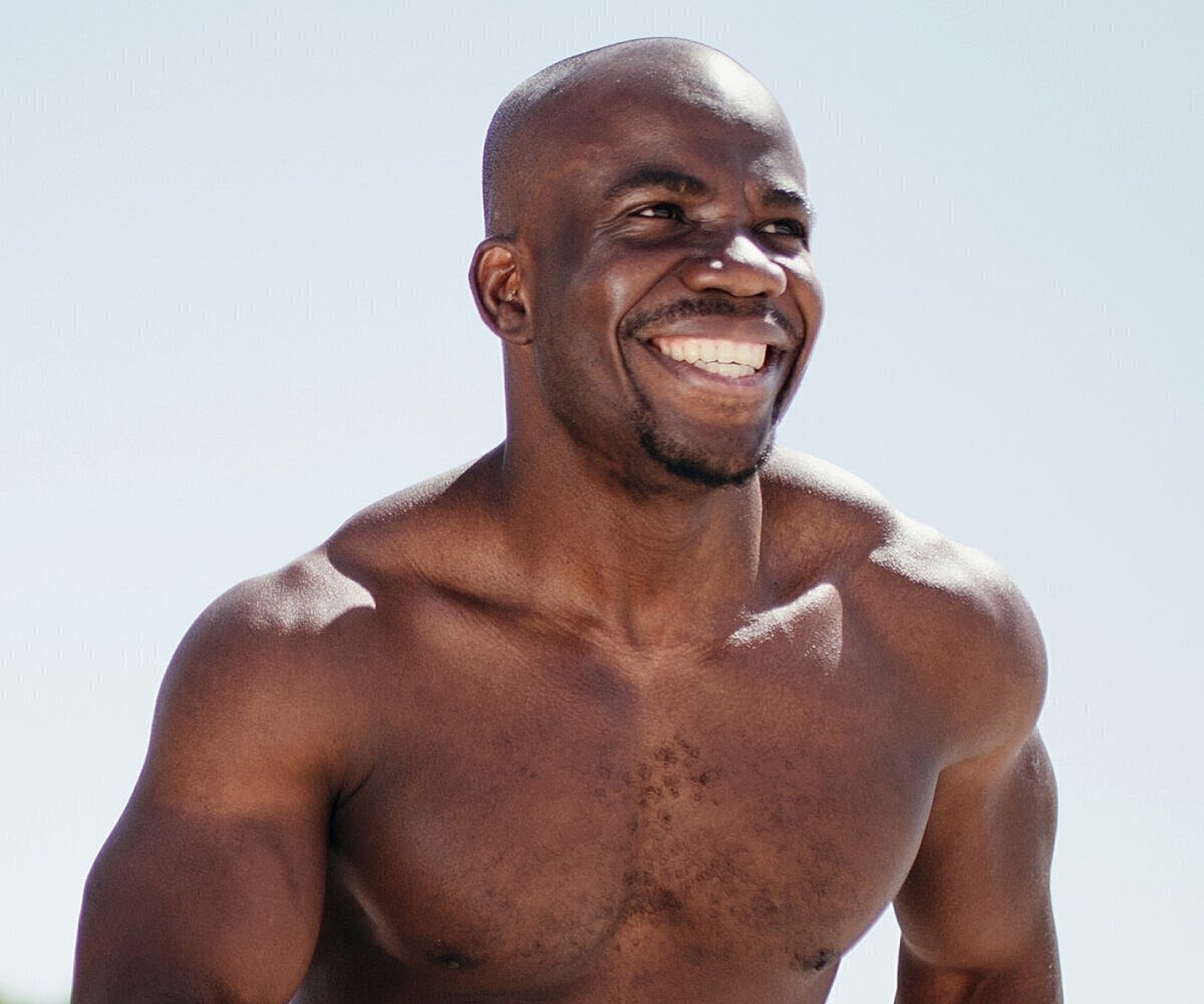 Smiling man running outdoors, shirtless and athletic.