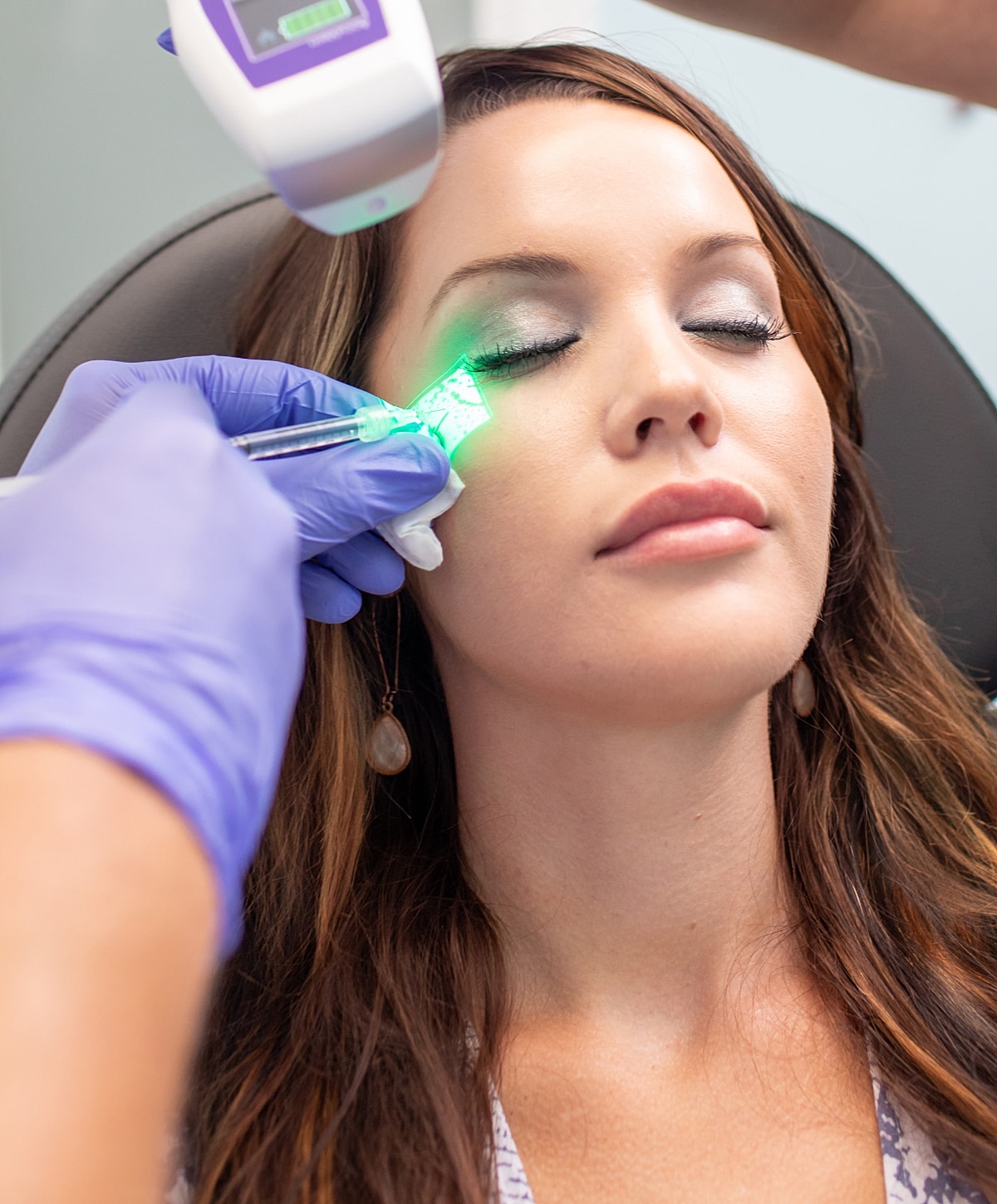 Woman receiving facial treatment with green light.