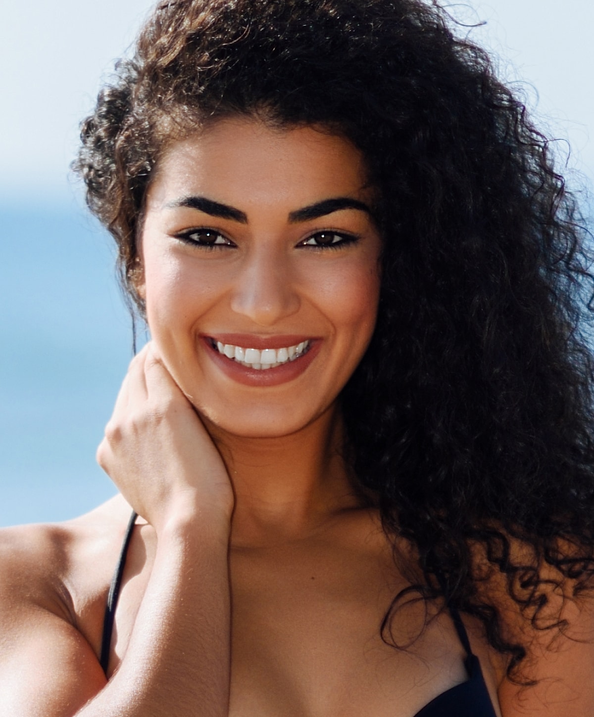Smiling woman with curly hair by the ocean.