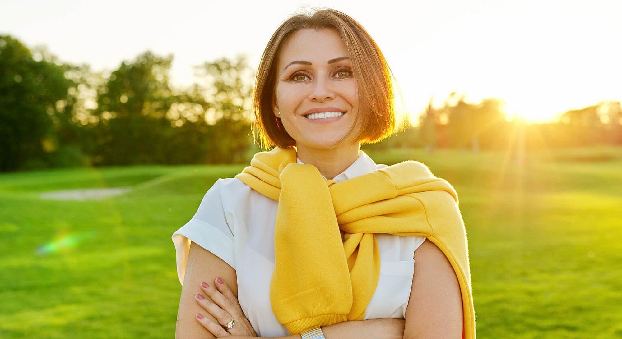 Woman smiling in a sunny outdoor setting.