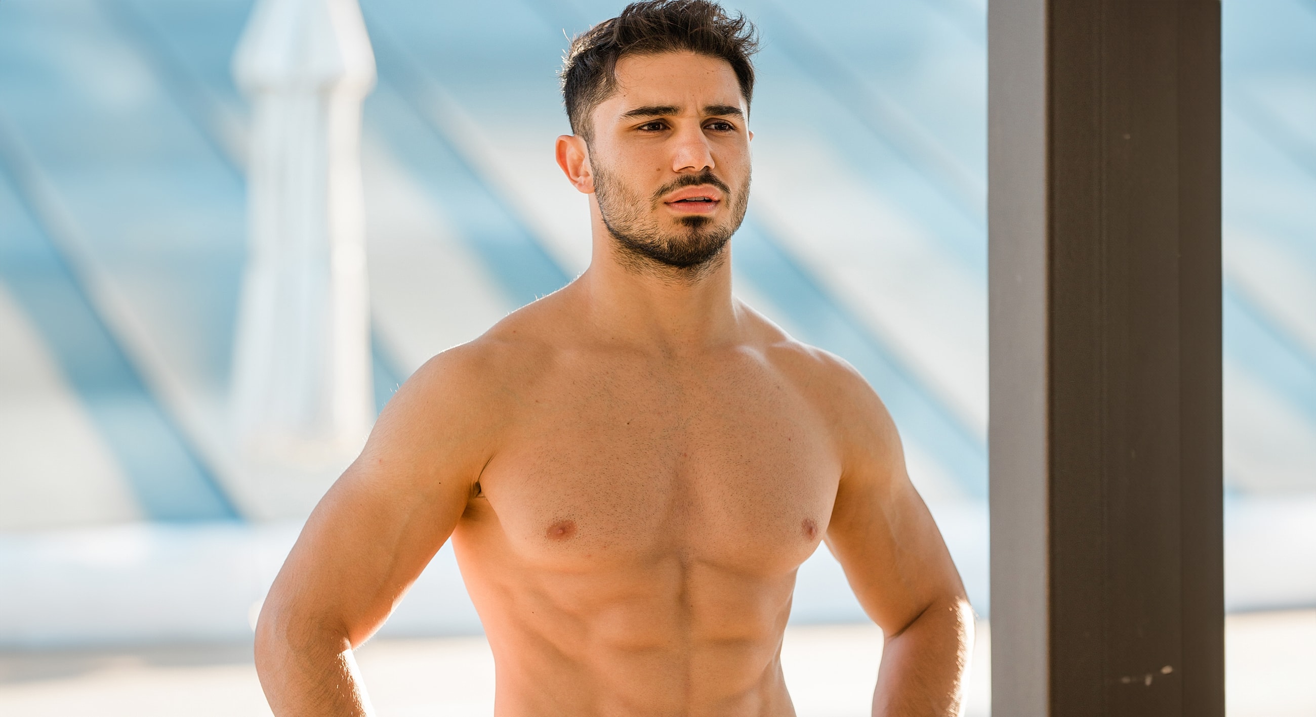 Man posing shirtless outdoors on a sunny day.
