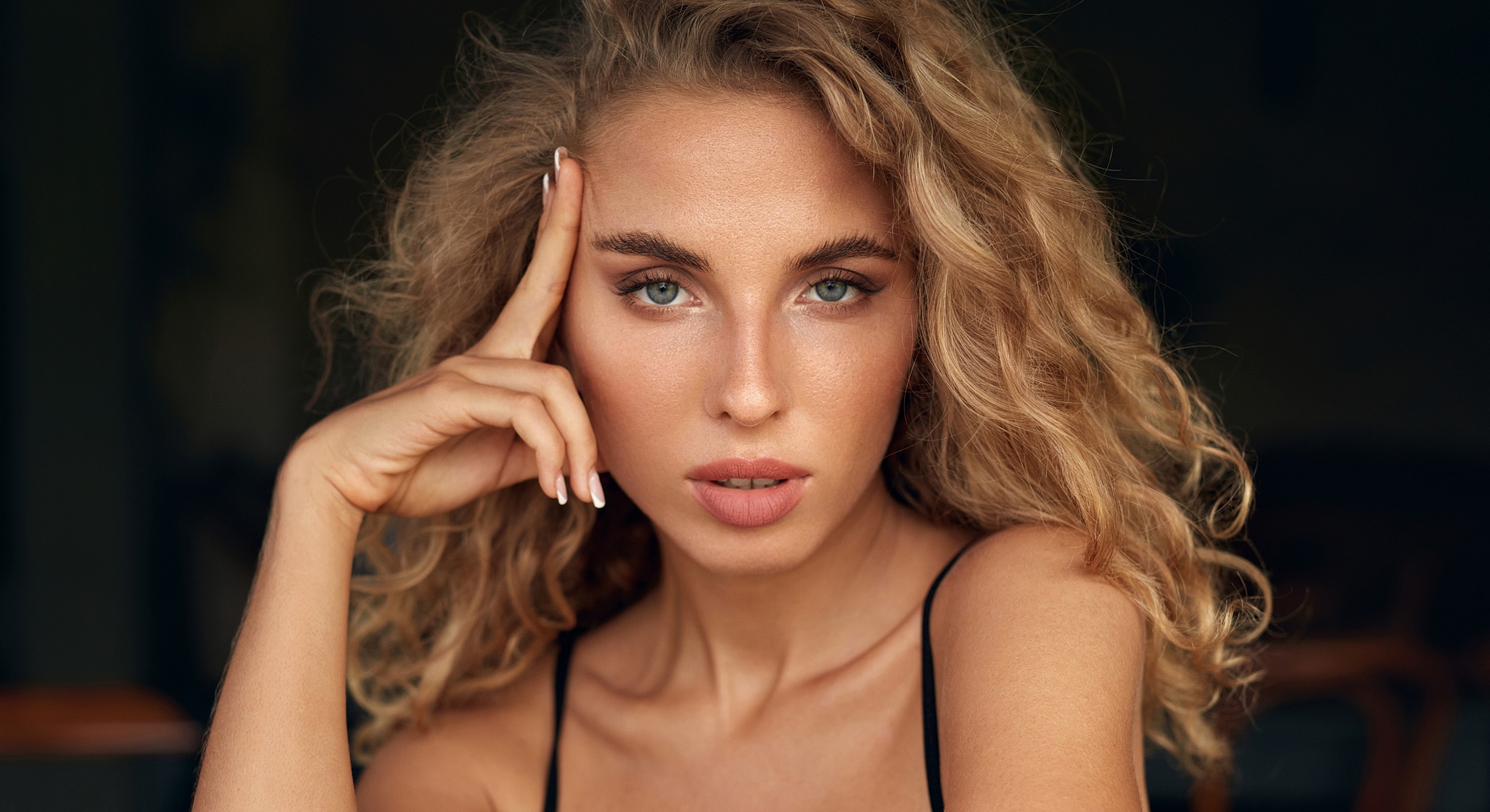 Woman with curly hair in thoughtful pose.